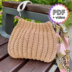 May include: A beige crochet handbag with a white strap and silver hardware. The bag has a ribbed texture and a rounded shape. A patterned scarf in pink, gold, and black is attached. The image includes text that says "PDF + video".