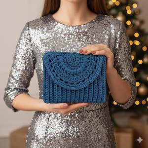 Op de afbeelding: Een blauwe gehaakte clutch met een klep. De tas heeft een geribbelde textuur op de body en een decoratief halfrond patroon op de klep. De clutch wordt vastgehouden voor een persoon die een zilveren paillettenjurk draagt.