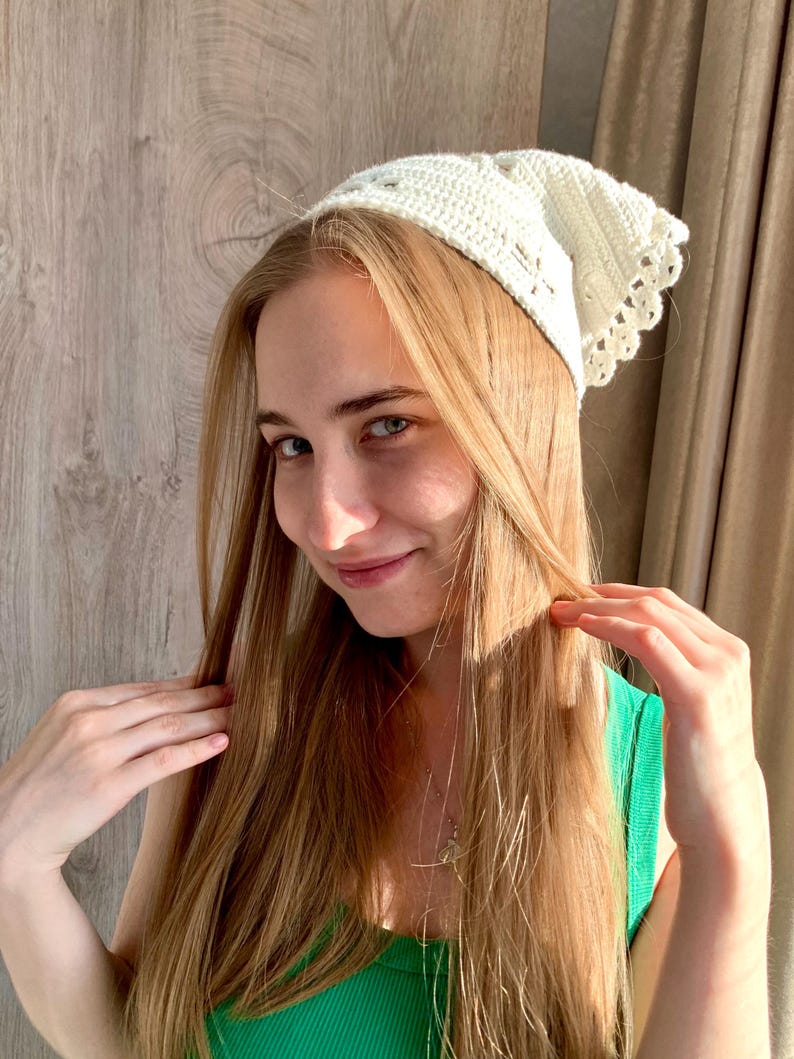 K&ouml;nnte beinhalten: Eine cremefarbene, geh&auml;kelte Kopfbedeckung mit einem gewellten Rand. Die Kopfbedeckung ist aus einem weichen, strukturierten Garn gefertigt und weist ein zartes Lochmuster auf. Der Artikel wird auf dem Kopf getragen.