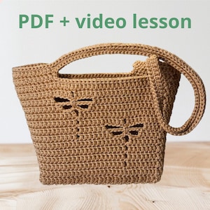 Op de afbeelding: Een bruine gehaakte tote bag met libellen uitsparingen. De tas heeft twee handvatten en een rechthoekige vorm. De tekst "PDF + video lesson" staat in de linkerbovenhoek.