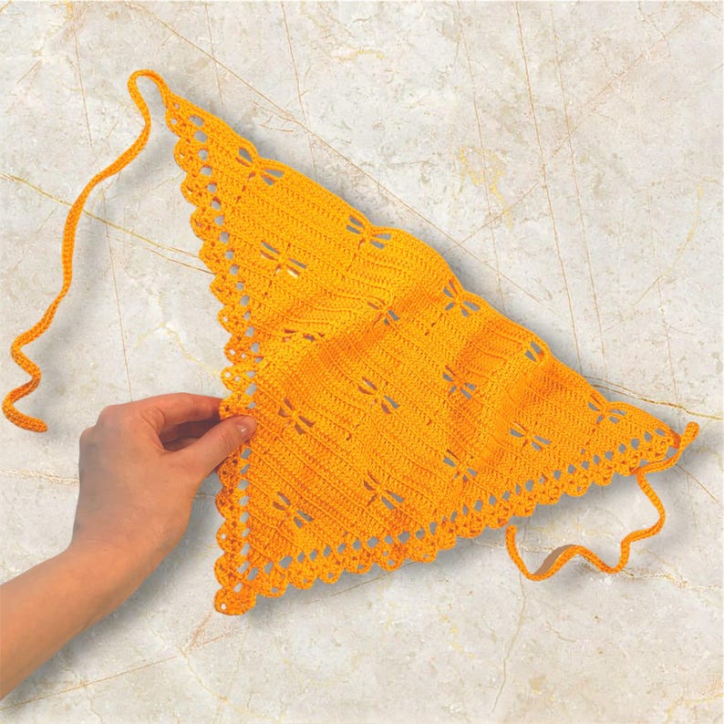 K&ouml;nnte beinhalten: Ein handgefertigtes, hellgelbes Dreieckstuch aus H&auml;kelarbeit. Der Schal hat einen gewellten Rand und Libellen-Ausschnitte. Der Schal wird von einer Hand gehalten, wobei die Bindeb&auml;nder sichtbar sind. Der Schal ist aus einem weichen, strukturierten Garn gefertigt.