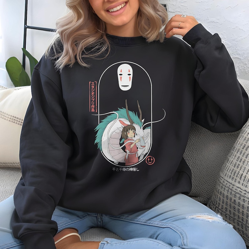 May include: Black sweatshirt featuring a graphic from the animated film, Spirited Away. The design includes the character No-Face, a dragon, and a girl in a red dress. Japanese text is also visible. The sweatshirt is a dark charcoal color.