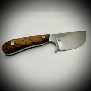 May include: A handcrafted knife with a wooden handle and a stainless steel blade. The handle is a light brown color with dark brown marbling. The blade has a curved edge and a small logo near the handle.