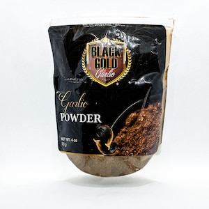 Op de afbeelding: Een zwarte en gouden zak met Black Gold knoflookpoeder, met een nettogewicht van 113 gram. De zak heeft een zwarte knoflookteentje en de tekst "Garlic Powder".