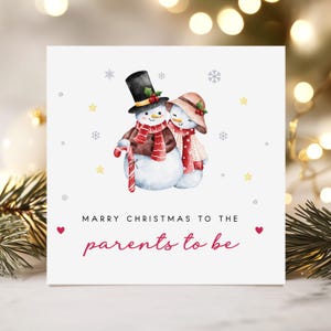May include: A Christmas card featuring a watercolour illustration of two snowmen. One snowman wears a black top hat and the other a pink hat. The card reads "Marry Christmas to the parents to be."