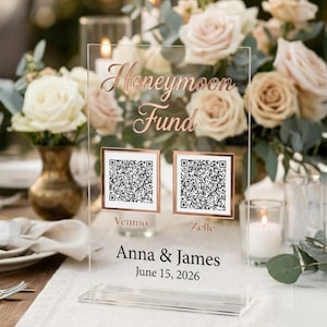 May include: Clear acrylic sign with rose gold lettering that reads "Honeymoon Fund." Below are two QR codes with "Venmo" and "Zelle" labels. The sign also includes the names "Anna & James" and the date "June 15, 2026."