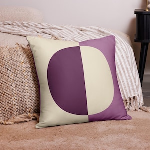 May include: A decorative throw pillow with a geometric design. The pillow is cream colored with a large purple half-circle on the front.
