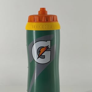 Op de afbeelding: Groene Gatorade waterfles met oranje en gele accenten. De fles toont het Gatorade logo en de tekst "TEAM BOBU". Ontworpen voor sport en hydratatie.
