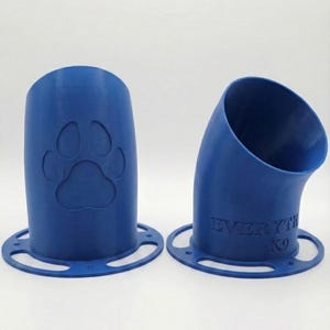 K&ouml;nnte beinhalten: Zwei blaue, 3D-gedruckte Hundeleckerli-Spender. Einer ist zylindrisch mit einem Pfotenabdruck, der andere ist gebogen mit dem Text "EVERYTHING K9". Beide haben eine kreisf&ouml;rmige Basis mit L&ouml;chern.