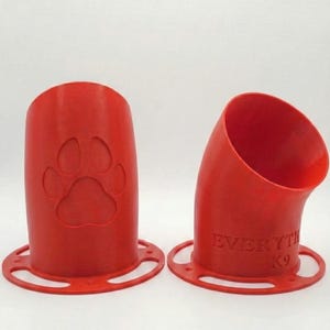 K&ouml;nnte beinhalten: Zwei rote, 3D-gedruckte Hundeleckerli-Spender. Einer hat einen Pfotenabdruck, der andere den Text "EVERYTHING K9". Beide haben eine kreisf&ouml;rmige Basis mit L&ouml;chern. Die Spender sind zylindrisch mit einer gebogenen &Ouml;ffnung.
