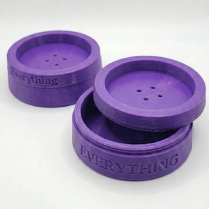 May include: Three purple, circular containers with lids. The word "Everything" is embossed on the side of each container. The lids have three small holes. One lid is off, revealing the inside of the container.
