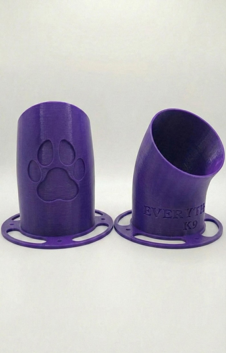 K&ouml;nnte beinhalten: Zwei lila 3D-gedruckte Hundeleckerli-Spender. Einer hat einen Pfotenabdruck, der andere den Text "EVERYTH K9". Beide haben eine kreisf&ouml;rmige Basis mit L&ouml;chern. Die Spender sind abgewinkelt und zylindrisch.
