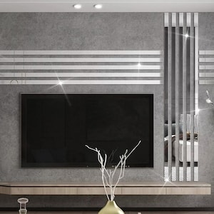 May include: A modern living room with a flat screen TV mounted on a wall with a grey background. The wall is decorated with a silver mirror tile design. The TV is on a wooden shelf with a vase of white branches and a gold vase.