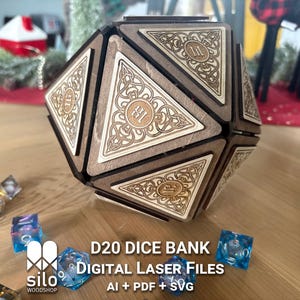May include: A wooden D20 dice bank with laser-cut designs. The bank is a dodecahedron shape with intricate Celtic knot patterns and the number 11 on each face. Several colourful dice are scattered around the bank. The text "D20 DICE BANK Digital Laser Files" is visible.