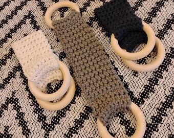 May include: Three crocheted teethers with wooden rings. The teethers are in beige, brown, and black. The rings are natural wood.
