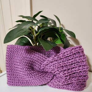 May include: A knitted purple headband with a twisted knot design. The headband is made of a thick, textured yarn and is displayed with a green plant in the background. The shop name "ThreeThreads" is visible at the bottom.