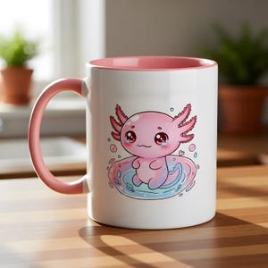 以下が含まれることがあります： ピンク色の内側とハンドルが付いた白いセラミックマグ。マグには、ピンク、青、赤のアホロートルイラストが描かれています。アホロートルは青とピンクの水たまりの中に座っています。