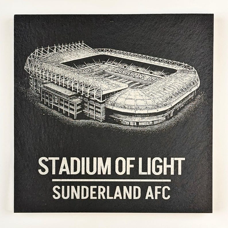 Puede incluir: Un posavasos cuadrado de pizarra negra con una ilustraci&oacute;n blanca grabada del Stadium of Light. El texto "STADIUM OF LIGHT" aparece sobre una l&iacute;nea horizontal, con "SUNDERLAND AFC" impreso debajo en una fuente blanca sin remates.