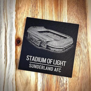 Puede incluir: Un posavasos cuadrado de pizarra negra con una detallada ilustraci&oacute;n grabada con l&aacute;ser en blanco del Stadium of Light. El texto STADIUM OF LIGHT y SUNDERLAND AFC est&aacute; impreso en letras may&uacute;sculas blancas debajo del gr&aacute;fico del estadio.