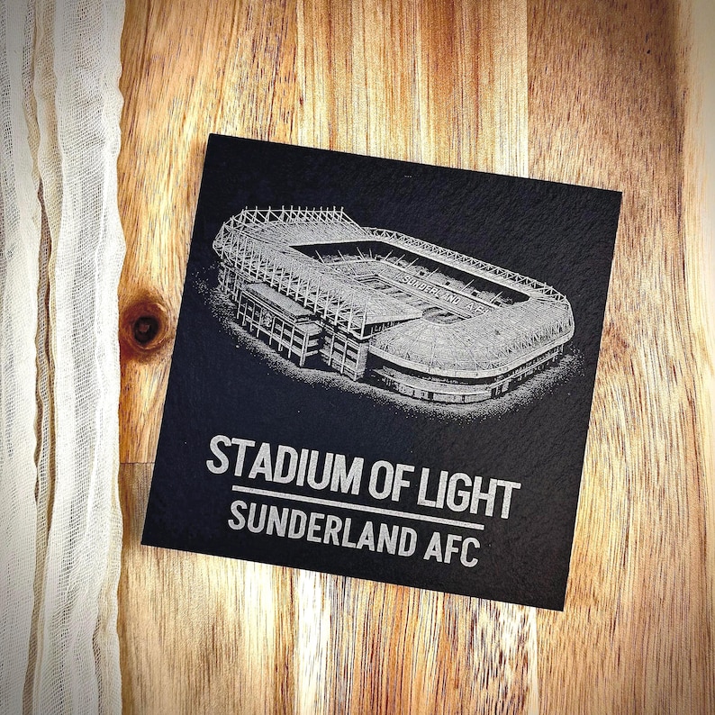 Puede incluir: Un posavasos cuadrado de pizarra negra con una detallada ilustraci&oacute;n grabada con l&aacute;ser en blanco del Stadium of Light. El texto STADIUM OF LIGHT y SUNDERLAND AFC est&aacute; impreso en letras may&uacute;sculas blancas debajo del gr&aacute;fico del estadio.