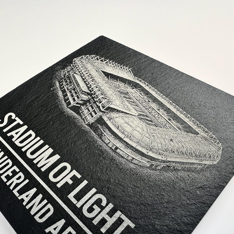 Puede incluir: Un posavasos cuadrado de pizarra negra con un grabado l&aacute;ser blanco detallado de una vista a&eacute;rea del Stadium of Light. El texto "STADIUM OF LIGHT" y "SUNDERLAND AFC" est&aacute; impreso en una fuente blanca sans-serif en la parte inferior izquierda.