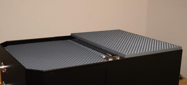 May include: A black box with a gray textured lid. The lid is slightly ajar, revealing the interior of the box, which is also lined with a gray textured material.