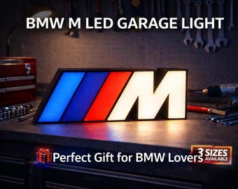 Peut inclure: Une enseigne lumineuse LED de garage BMW M rectangulaire arborant le logo M aux couleurs bleu, bleu foncé, rouge et blanc. Le panneau est éclairé par un système interne et affiche le texte BMW M LED GARAGE LIGHT en haut.