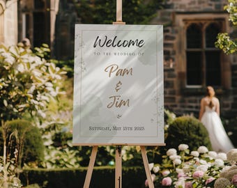May include: A wooden easel displays a wedding welcome sign. The sign reads "Welcome" and announces the wedding of Pam & Jim, with the date Saturday, May 13th, 2023. The background includes a garden and a bride in a white dress.
