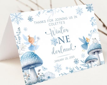 May include: A blue and white thank you card with a winter wonderland theme. It features two fairies sitting on mushrooms with snowflakes and floral accents. The text reads "Thanks for joining us in Colette's Winter Wonderland, January 25, 2025."