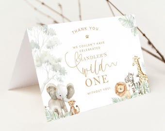 May include: A folded white card with a safari theme. The card features an illustration of an elephant, lion, zebra, and giraffe. Text on the card reads "Thank You", "Chandler's Wild One", and "We couldn't have celebrated without you!"