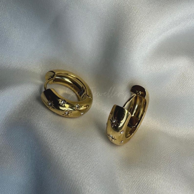 May include: A pair of gold hoop earrings with a star design. The earrings are made of metal and have a shiny finish.