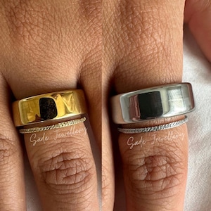 May include: Two rings are shown on fingers. One is a wide, gold band, and the other is a wide, silver band. Below each wide band is a thin ring with small, clear stones. The text "Sade Jewellery" is written below the rings.