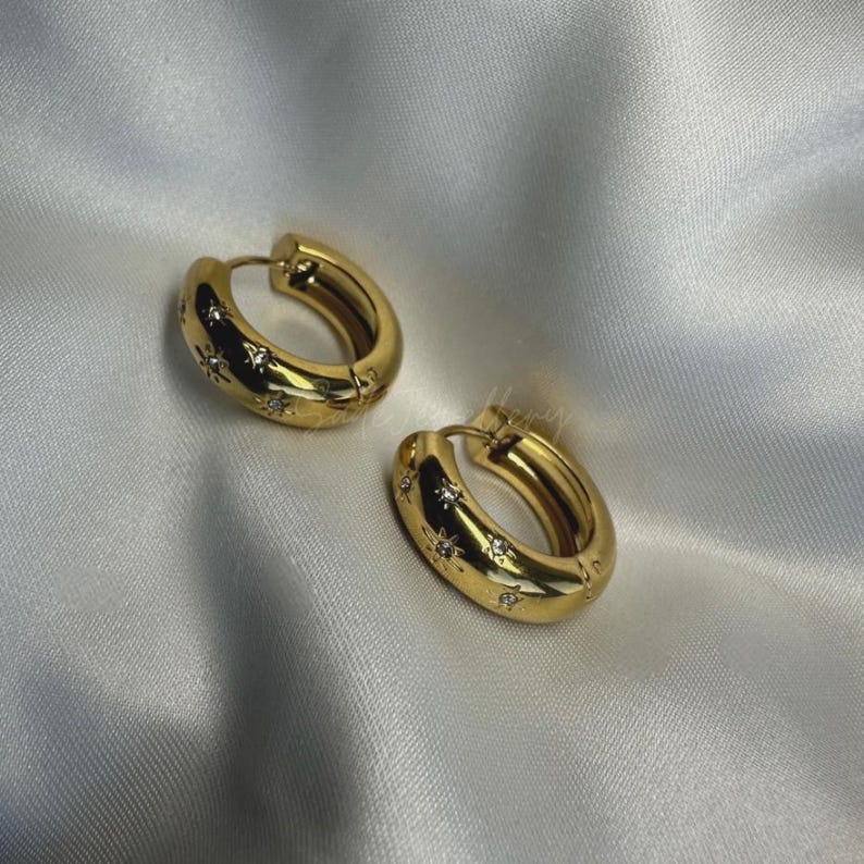 May include: Gold hoop earrings with a star design and clear rhinestones.