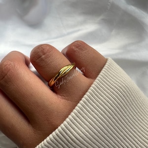 May include: A gold-toned ring with a twisted design. The ring is worn on a person's finger.