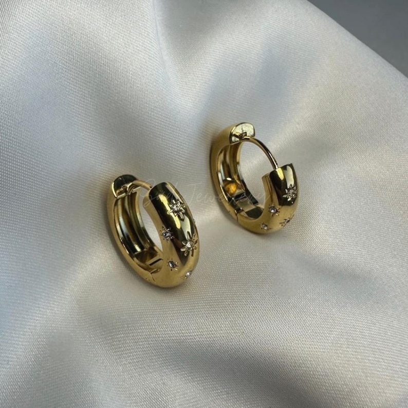 May include: Gold hoop earrings with a star design. The earrings are made of metal and have a shiny finish.