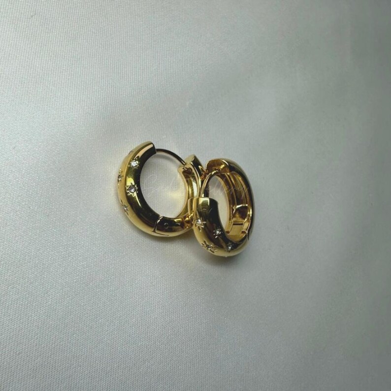 May include: A pair of gold hoop earrings with small clear stones set around the hoops.