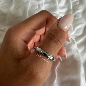 Op de afbeelding: Een zilveren ring met kleine, heldere edelstenen in de band. De ring wordt aan een vinger gedragen. De tekst "Safe Jewellery" staat op de ring.