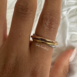 Puede incluir: Juego de anillos de tres bandas en tonos oro, oro rosa y plata. Los anillos están apilados en un dedo, mostrando los diferentes colores metálicos. Los anillos son sencillos y elegantes, adecuados para el uso diario.