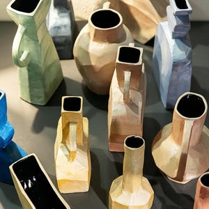 Könnte beinhalten: Eine Sammlung verschiedener Keramikvasen in unterschiedlichen Formen und Pastellfarben wie Hellgrün, Hellgelb, zartem Rosa und Hellblau. Jede Vase zeichnet sich durch eine geometrische Form, eine glatte Glasur und ein tiefschwarzes Inneres aus.