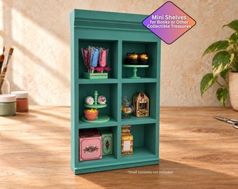 May include: A teal wooden display unit with six square compartments. The unit features a decorative top molding and contains various miniature items on its shelves. Text on the unit reads: Mini Shelves for Books or Other Collectible Treasures.