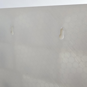 May include: Close-up of a white, textured surface with two small, raised, teardrop-shaped protrusions. The surface has subtle diagonal lines and a slightly uneven texture, suggesting a manufactured material.