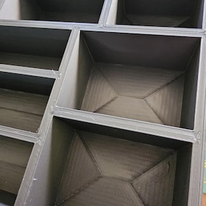K&ouml;nnte beinhalten: Ein modulares, dunkelgraues Aufbewahrungselement mit mehreren F&auml;chern. Das Element ist mit geraden Linien und rechten Winkeln konstruiert, wodurch ein geometrisches Muster entsteht. Das Innere jedes Fachs hat ein strukturiertes Aussehen.