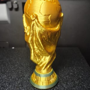 May include: A gold-colored trophy with a globe on top and a figure holding it. The base is green and gold. The trophy is likely a representation of a sports championship.