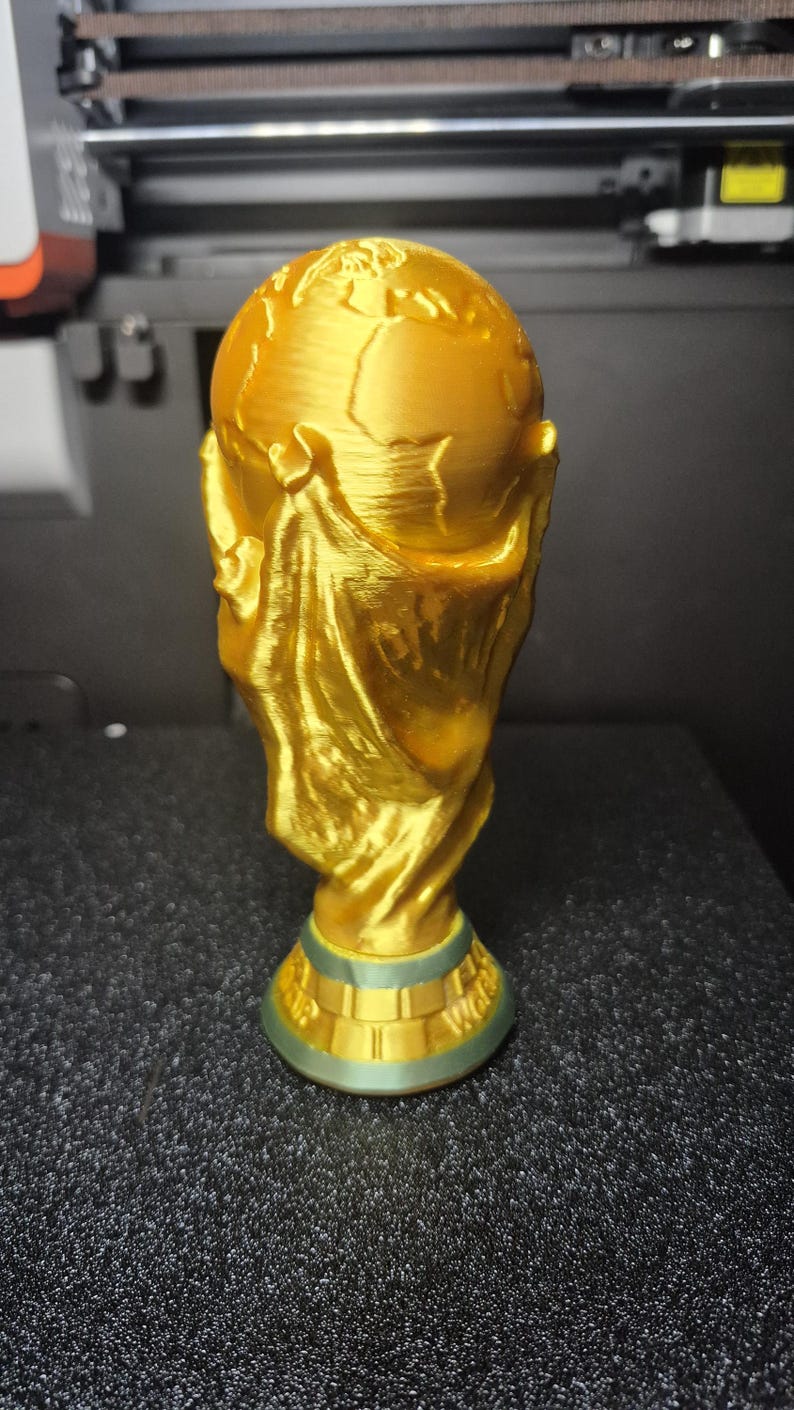 May include: A gold-colored trophy with a globe on top and a figure holding it. The base is green and gold. The trophy is likely a representation of a sports championship.