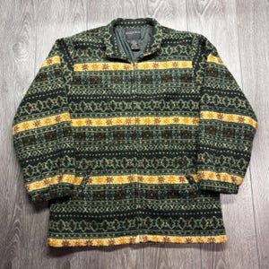 Könnte beinhalten: Eine grün-gelb gemusterte Jacke mit Reißverschluss und Stehkragen. Die Jacke hat ein sich wiederholendes geometrisches Design mit gelben sternartigen Formen und horizontalen Streifen. Der Markenname "SEQUENCE" ist am Kragen sichtbar.