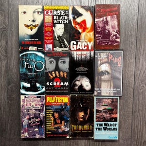 Peut inclure: Une collection de cassettes VHS vintage de films d'horreur et de suspense. Les titres incluent "Le Silence des Agneaux", "Scream 2" et "Candyman". Les cassettes sont disposées sur une surface en bois.