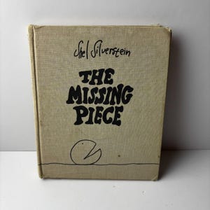 以下が含まれることがあります： シェル・シルヴァスタイン著「The Missing Piece」というタイトルのハードカバー本。本の表紙は薄いタン色で、黒い文字と、欠けた部分のある円のシンプルなイラストが描かれています。