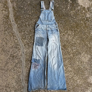 Peut inclure: Salopette en jean bleu clair avec une coupe large, une poche sur le plastron et des bretelles réglables. Le vêtement présente deux empiècements distincts sur la jambe gauche, l'un bleu uni et l'autre avec un motif floral bleu foncé.