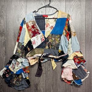 Könnte beinhalten: Ein Patchwork-Top mit V-Ausschnitt und langen Ärmeln. Das Oberteil besteht aus verschiedenen Stoffflicken in verschiedenen Farben und Mustern, darunter Blumen- und Unidesigns. Die Ärmel haben ein Rüschendetail.