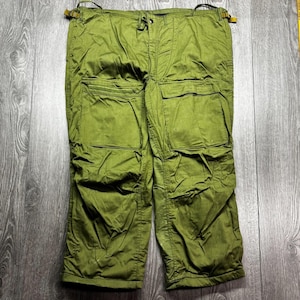 May include: Olive green cargo trousers with multiple pockets and adjustable straps. The trousers have a drawstring waist and are made of a durable fabric. The trousers are a cropped length.